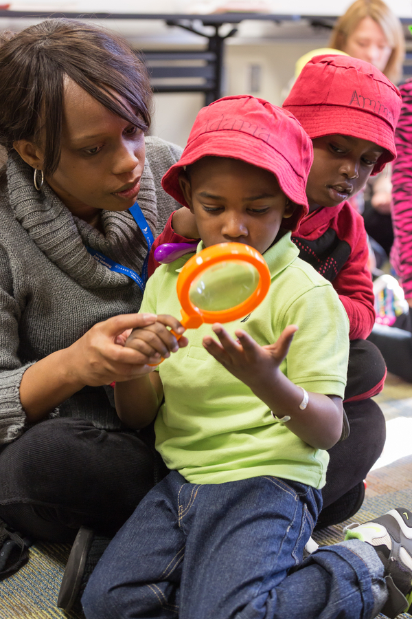 A teacher and young boy using a large magnifying glass to see things close up.