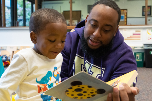 A man helps a young boy read a book.