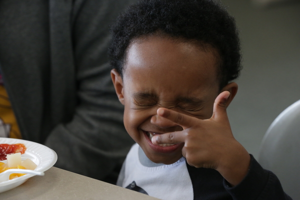 Young boy squinting and smiling while making finger gestures.