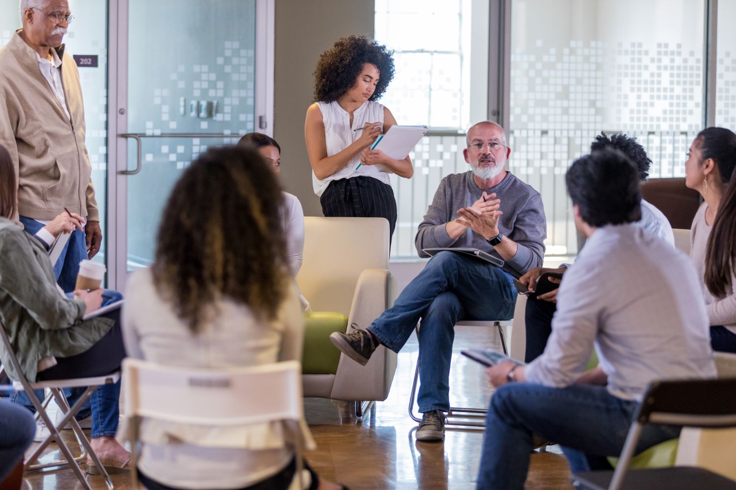 Varias personas reunidas para una reunión y algunas tomando notas.