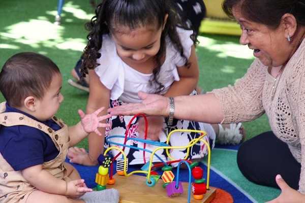 Teacher interacting with an infant and a preschooler outdoor.