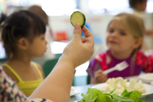 Children looking at an adult holding up a cucumber slice.