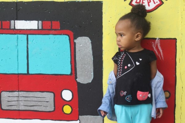 Niña de pie junto a una imagen pintada de un camión de bomberos.