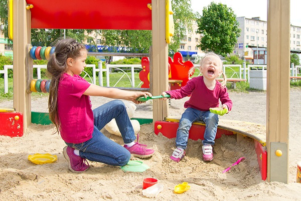 Kids in sandbox pulling at same toy.