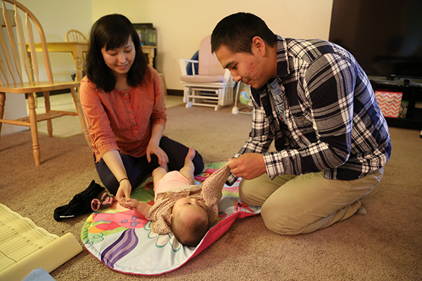 Parents changing diapers to a baby in a room floor.