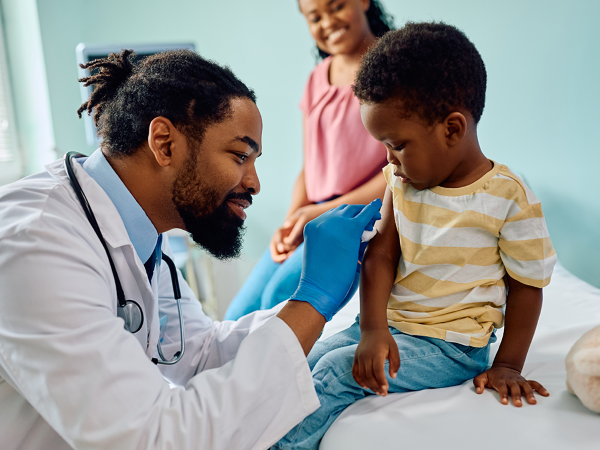 Una madre sonriente observa cómo el médico se prepara para vacunar a su hijo.