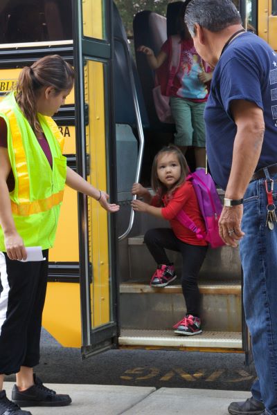 Niño bajando de un autobús escolar mientras sus padres están esperando.