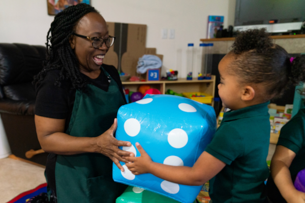 Maestra y niña jugando con un gran dado inflable azul.