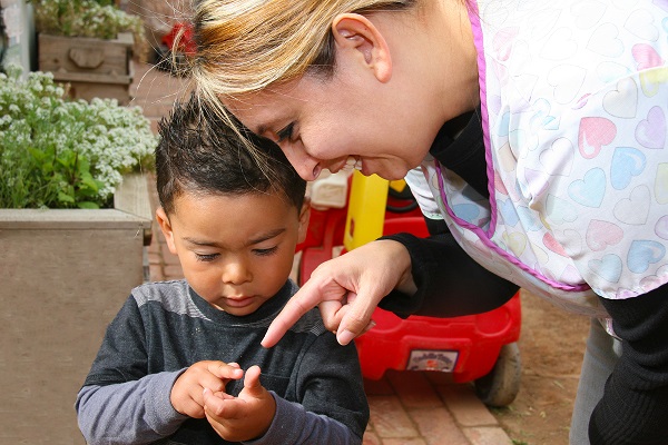 Teacher with a child outdoors, pointing to something in the child hands.