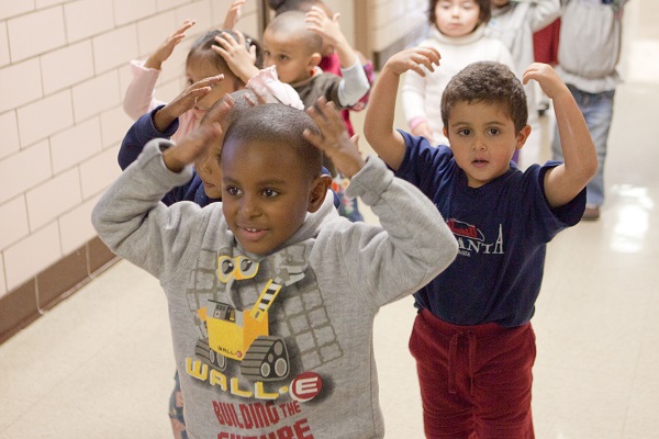 Children walking the hallway in line, with their hands up.