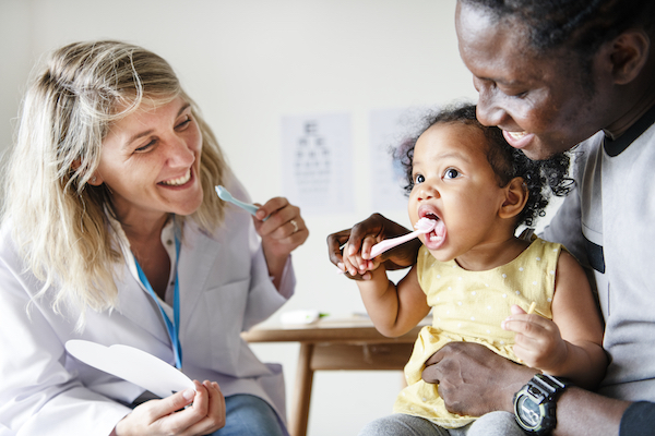 Dentist and parent showing a child how to use a toothbrush.