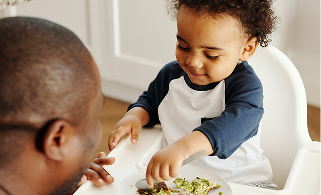 Toddler sitting in a chair while eating, in the presence of the caregiver.