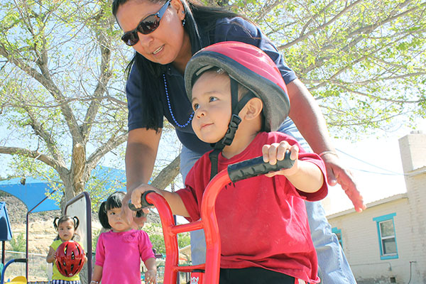 Docente ayudando a un niño a andar en triciclo.