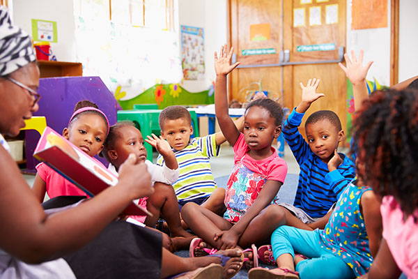 Children raising their hands during circle time at a child care classroom.