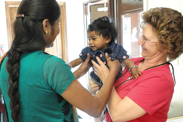 Una profesional de la salud levantando a un niño de las manos de una mujer.