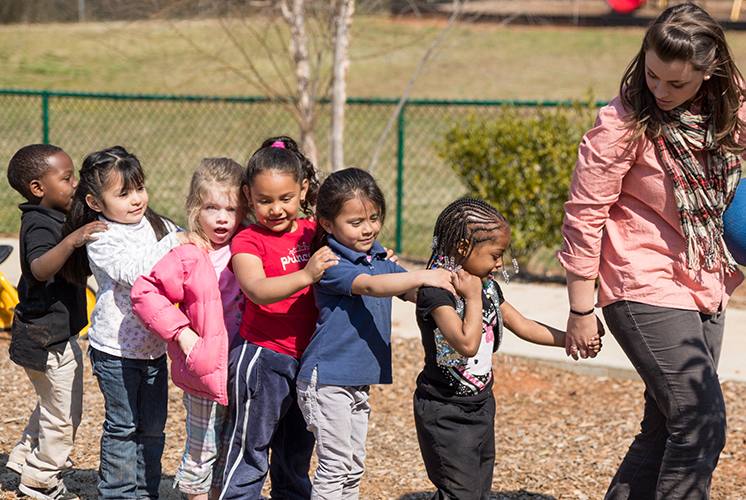 an adult leading a line of children outside