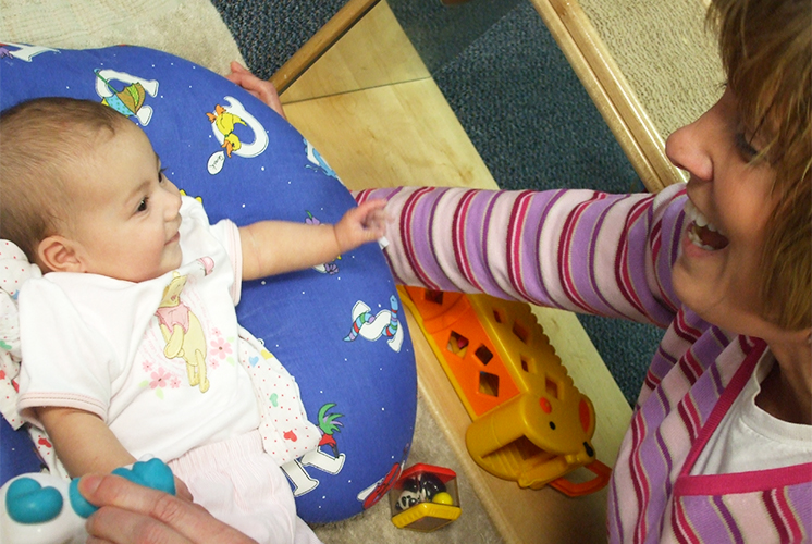 A woman smiles at baby lying on carpet