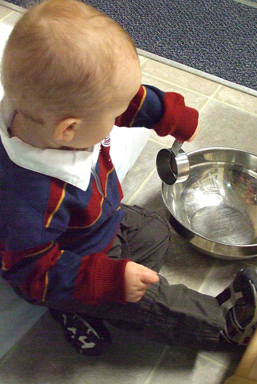 a boy plays with measuring cup and bowl