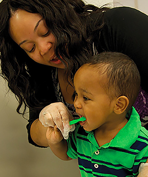 women helping child brush teeth