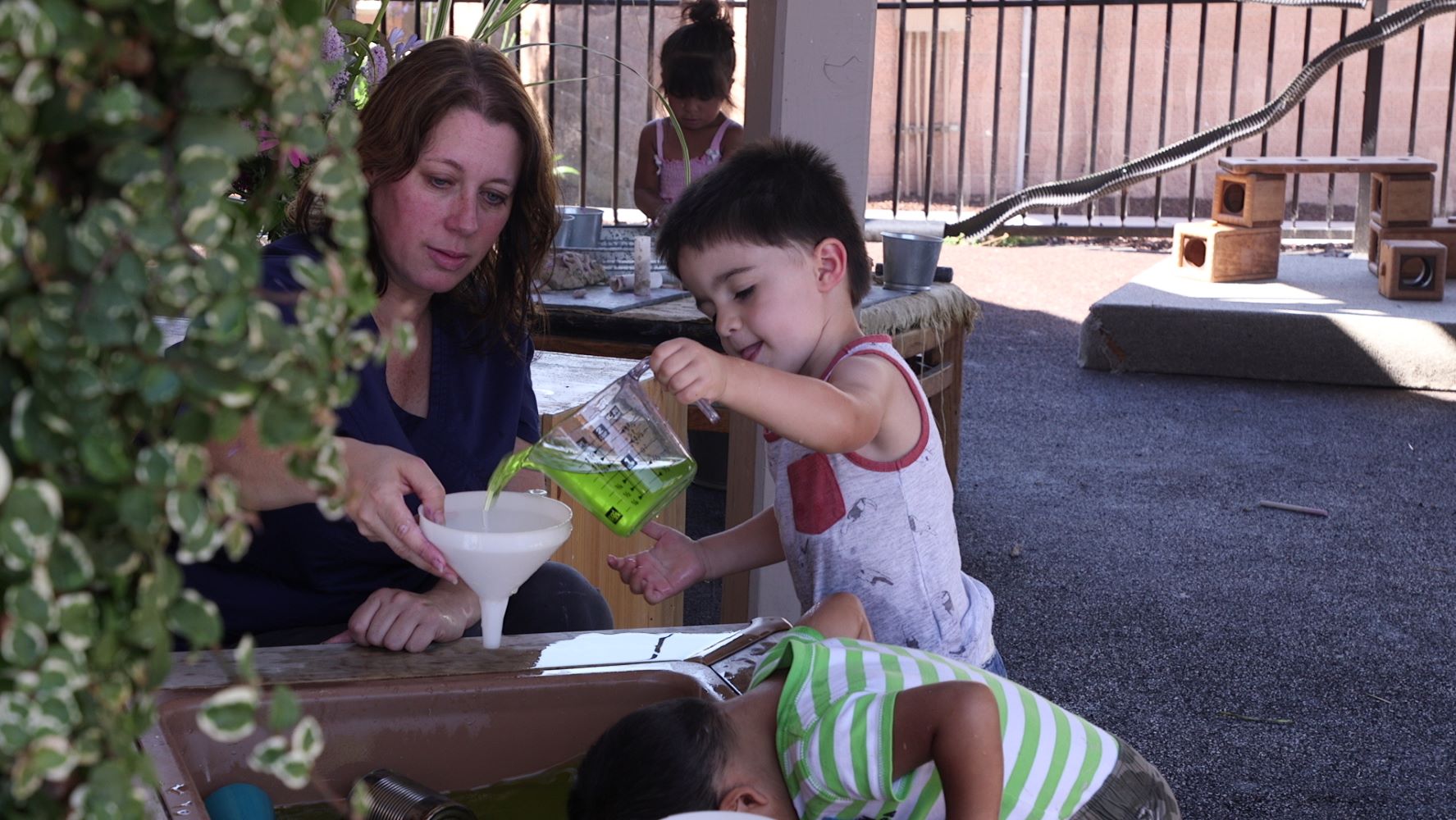 Child pouring liquid into a funnel being held by an adult.