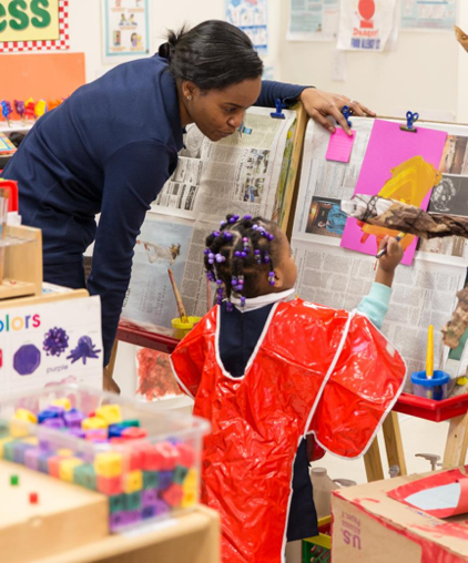 Teacher watching child put finishing touch on her artwork.