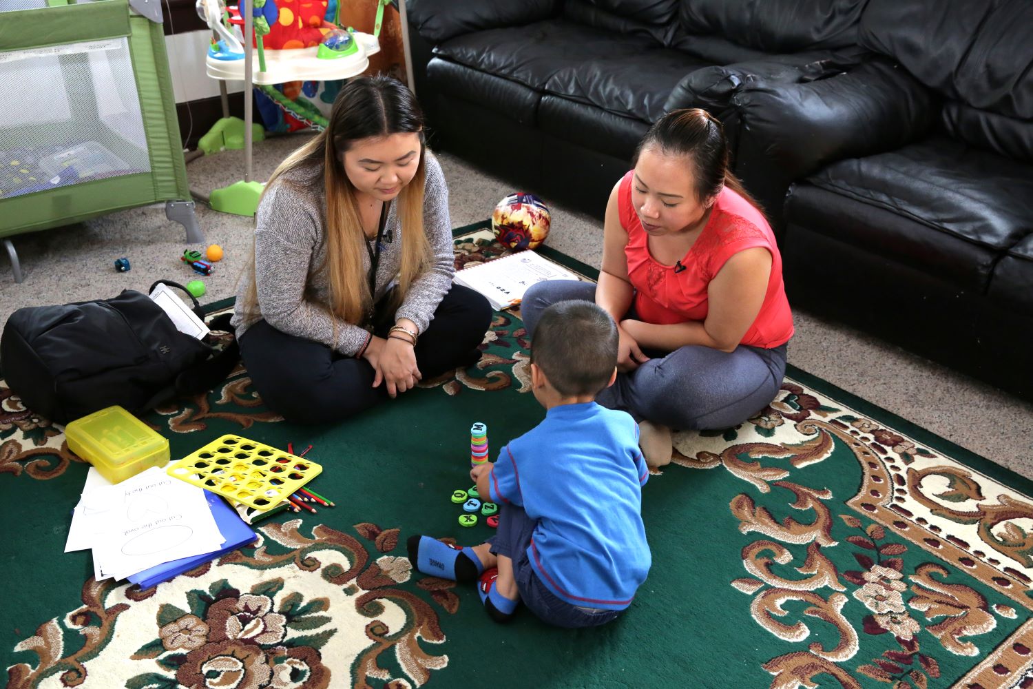 Two women watching as young boy stacks colored discs.