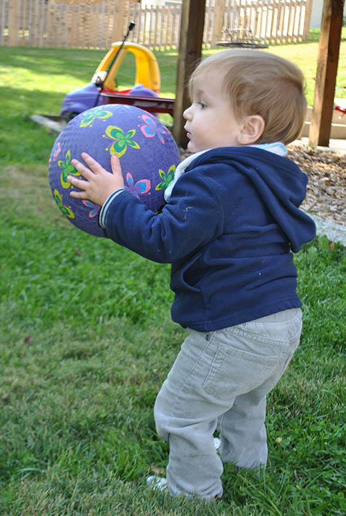 a boy stands on grass lawn holding a ball