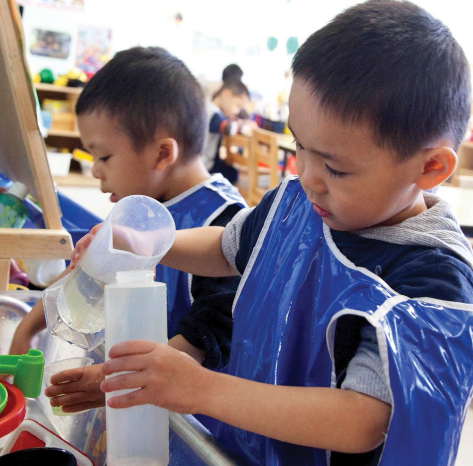 Two boys pour water between plastic beakers