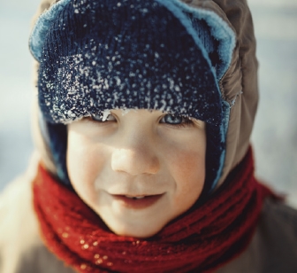 Un niño pequeño con abrigo pesado, bufanda y sombrero.