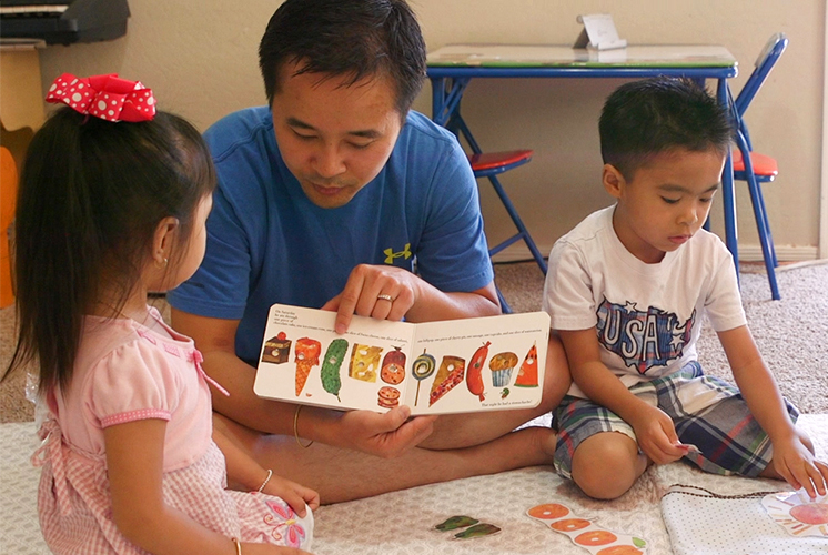 A father reads with daughter and son