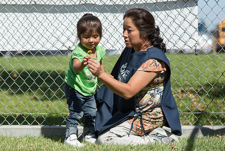 a teacher helps a girl examine a dandelion on the lawn