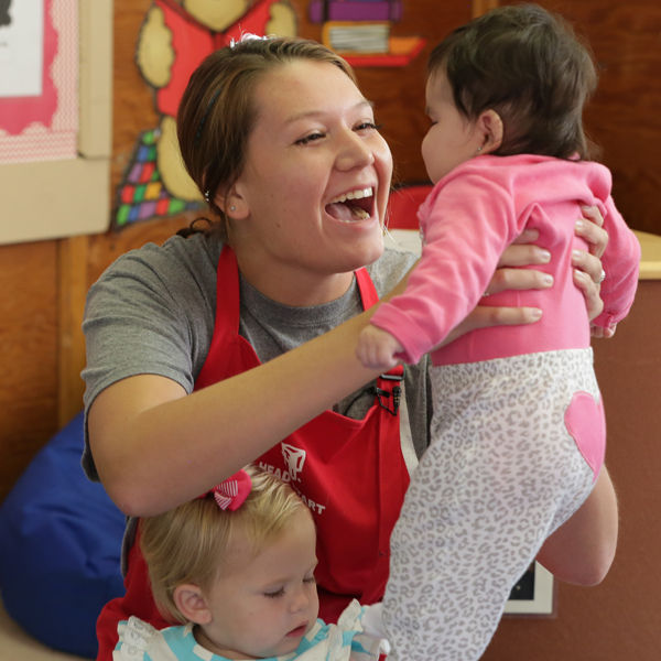 Head Start Teacher holding up one baby with another sitting in her lap