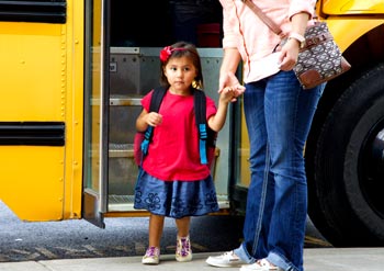 girl with adult next to school bus