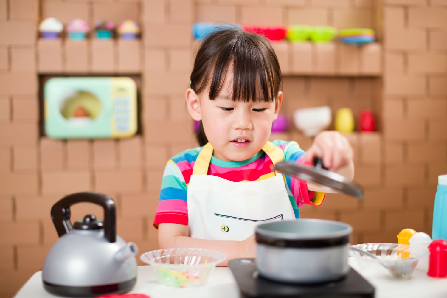 Young girl playing with pretend toy tea kettle and stovetop with pot.