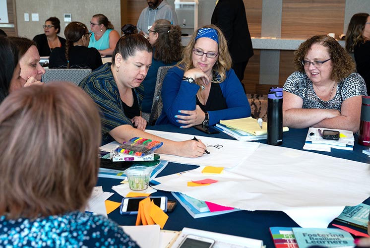 Adults around a conference table take notes with markers on large sheets of paper.