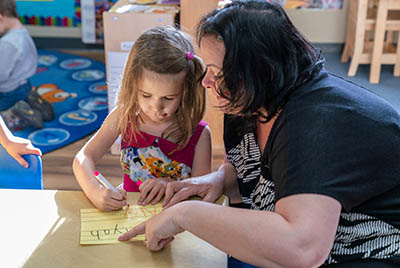 una maestra supervisa a una niña que está escribiendo letras