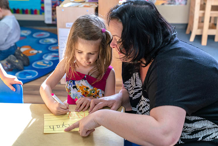 una maestra ayuda a una niña a escribir letras