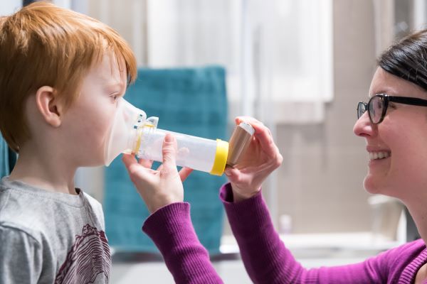 Young boy being assisted by an adult on how to use an asthma inhaler.