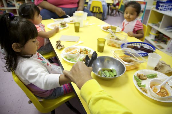 Point of view of an adult handing a salad tong to a child so they can serve themselves.