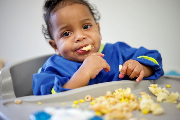 A child in a high chair placing food in their mouths.