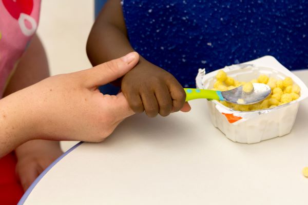 An adult guiding a child's hand while holding a spoon.