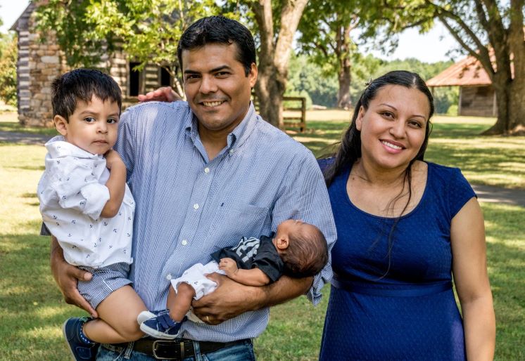 Mamá con un papá que tiene un bebé y un niño pequeño en cada brazo.