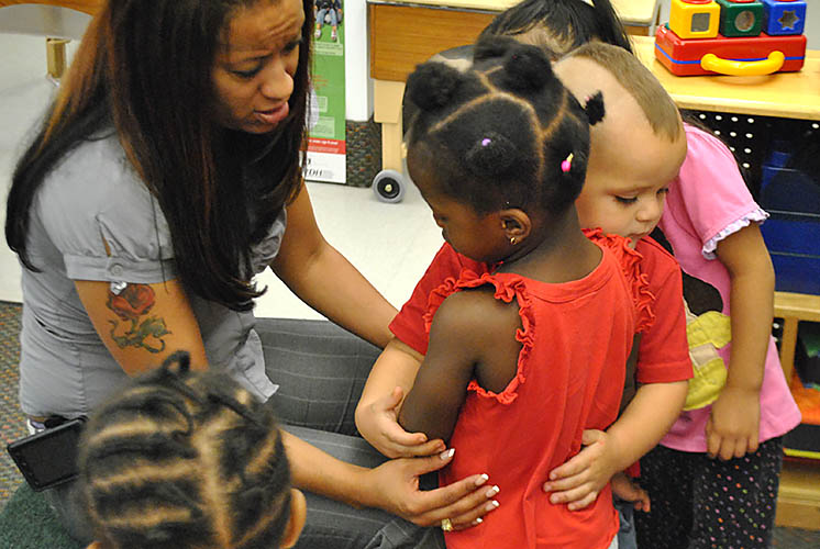 two children hug while a woman watches over them