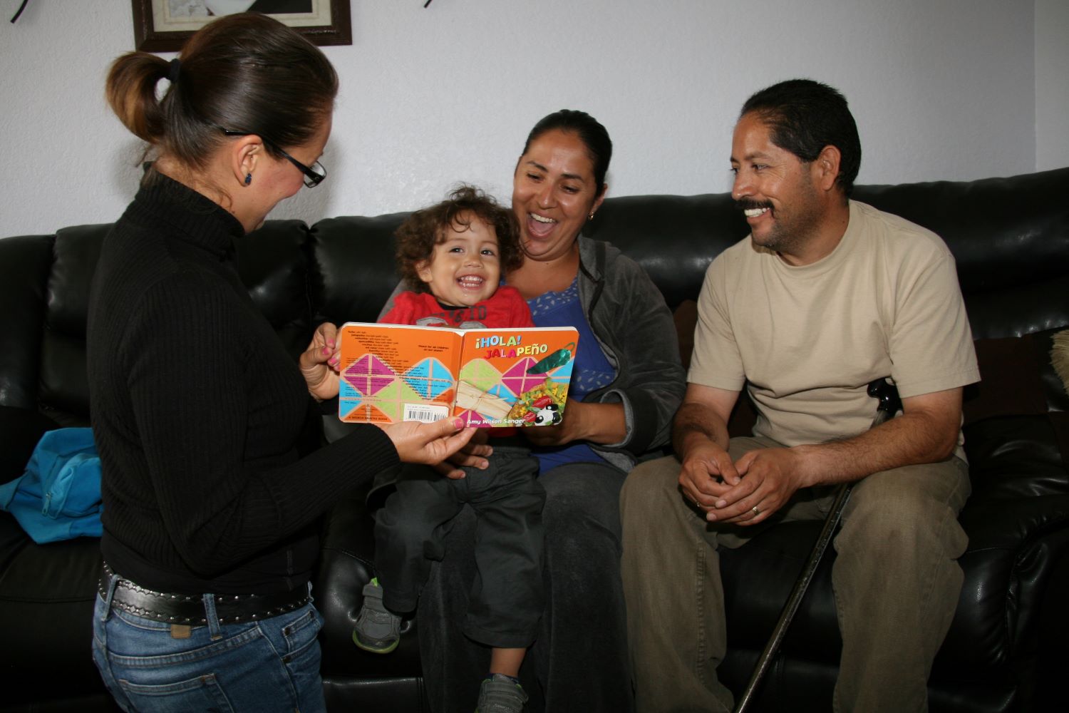 Visitadora del hogar con un niño y sus padres mirando un libro.