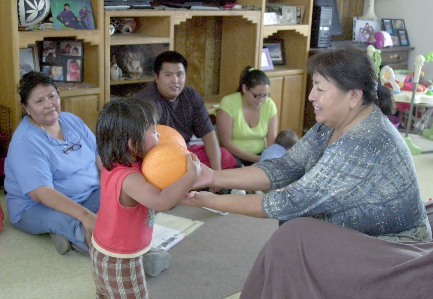 Adulto dando a niño una bola grande, mientras que otros adultos toman notas.