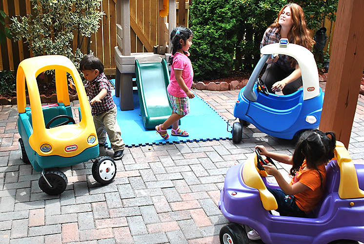 mientras que un adulto supervisa, los niños juegan al aire libre en el patio dentro de unos carritos de juguete móviles