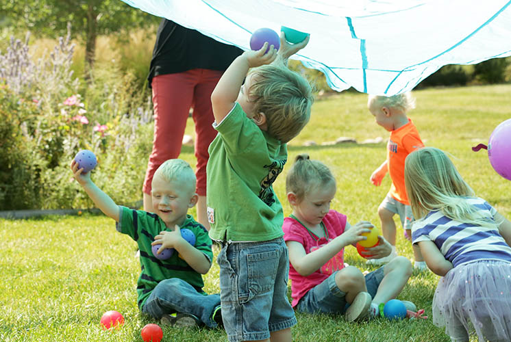 Kids play on the grass while adults hold parachute cloth up over their heads