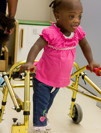 Little girl in pink shirt uses walker