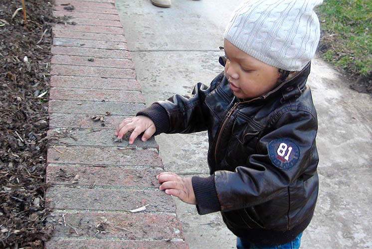 A boy in in warm clothes is outside examining brick planter wall