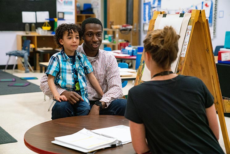 un padre sosteniendo a su hijo tiene una charla con un maestro